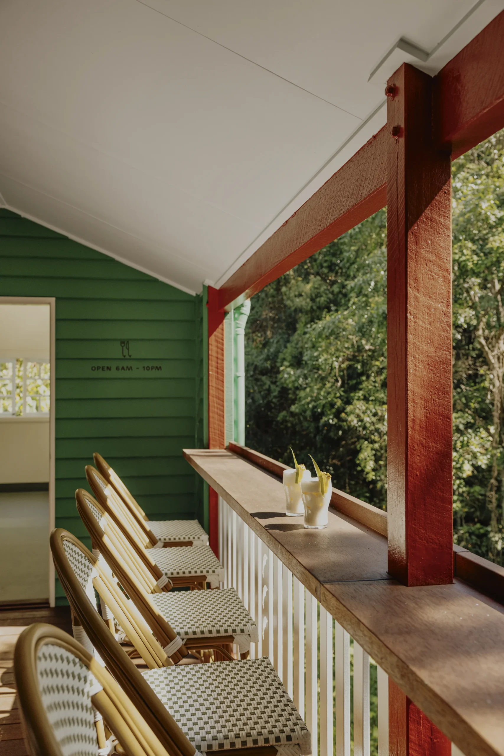 Cane chairs along a jungle-view balcony with cocktails on the rail, green cottage exterior