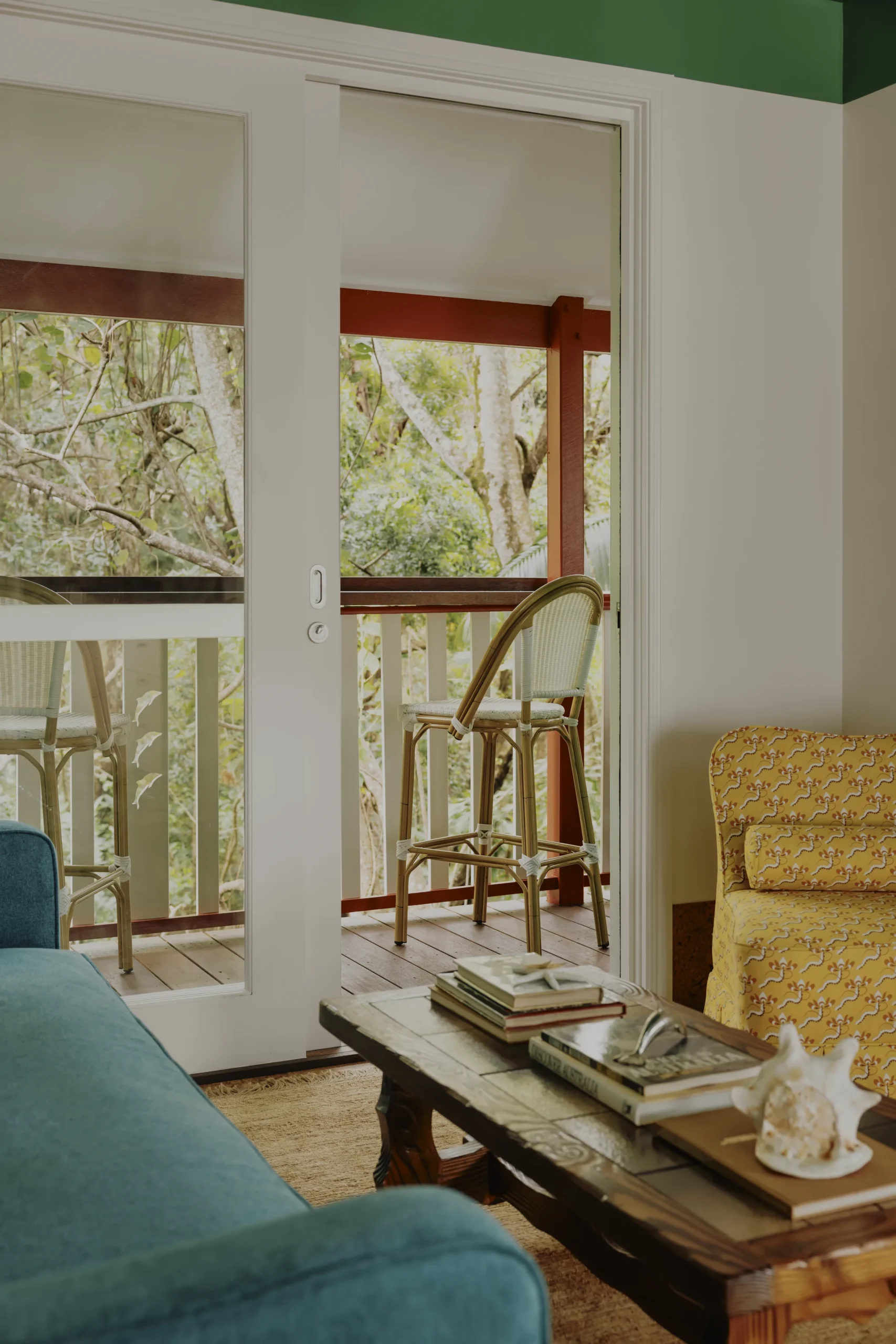 Living room with teal sofa and yellow armchair, sliding doors open to rattan balcony seating