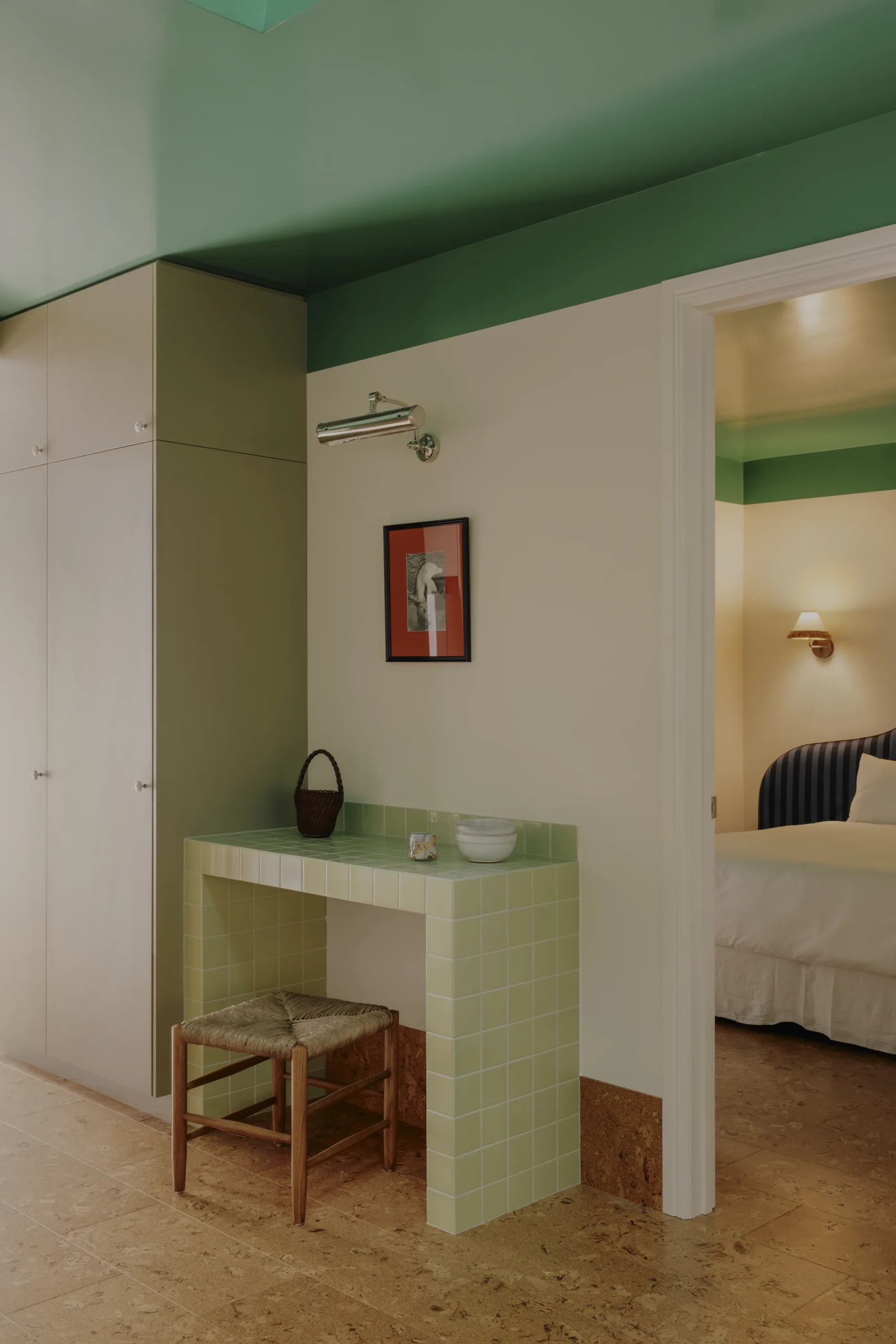 Green-ceilinged ensuite nook with tiled vanity, stool and stool, doorway to striped-headboard bedroom