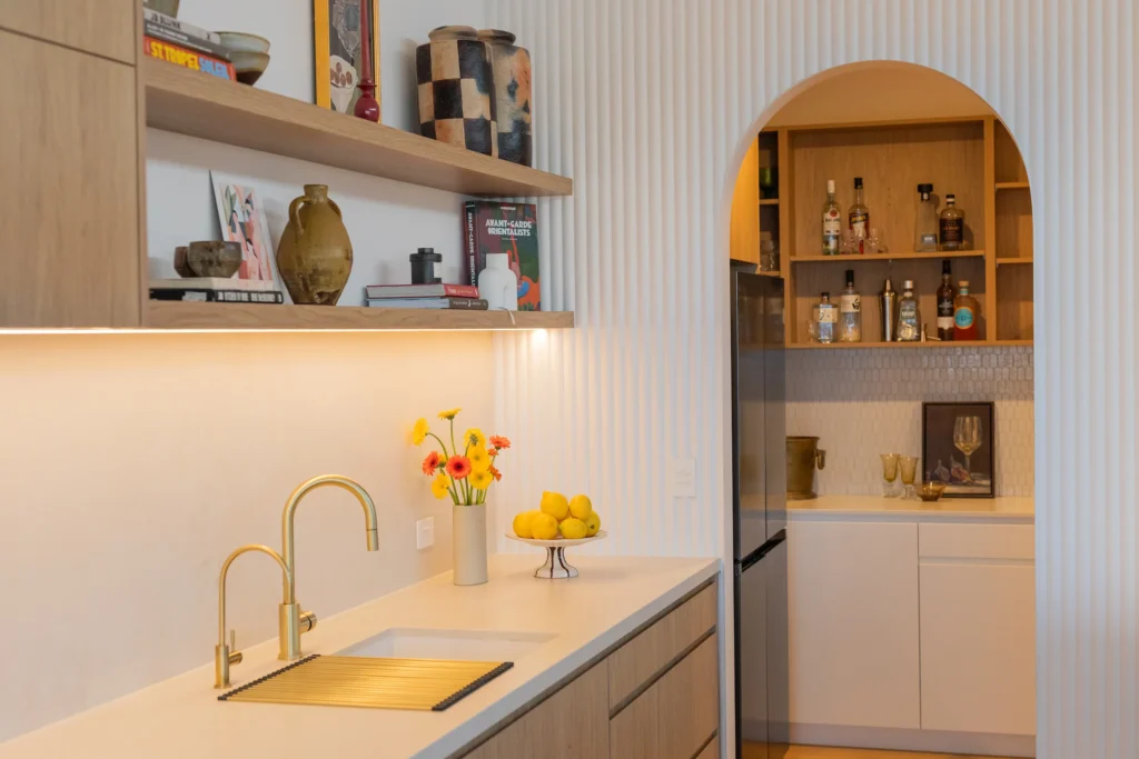 Kitchen with brass tapware, open shelving and archway to a timber cocktail bar nook