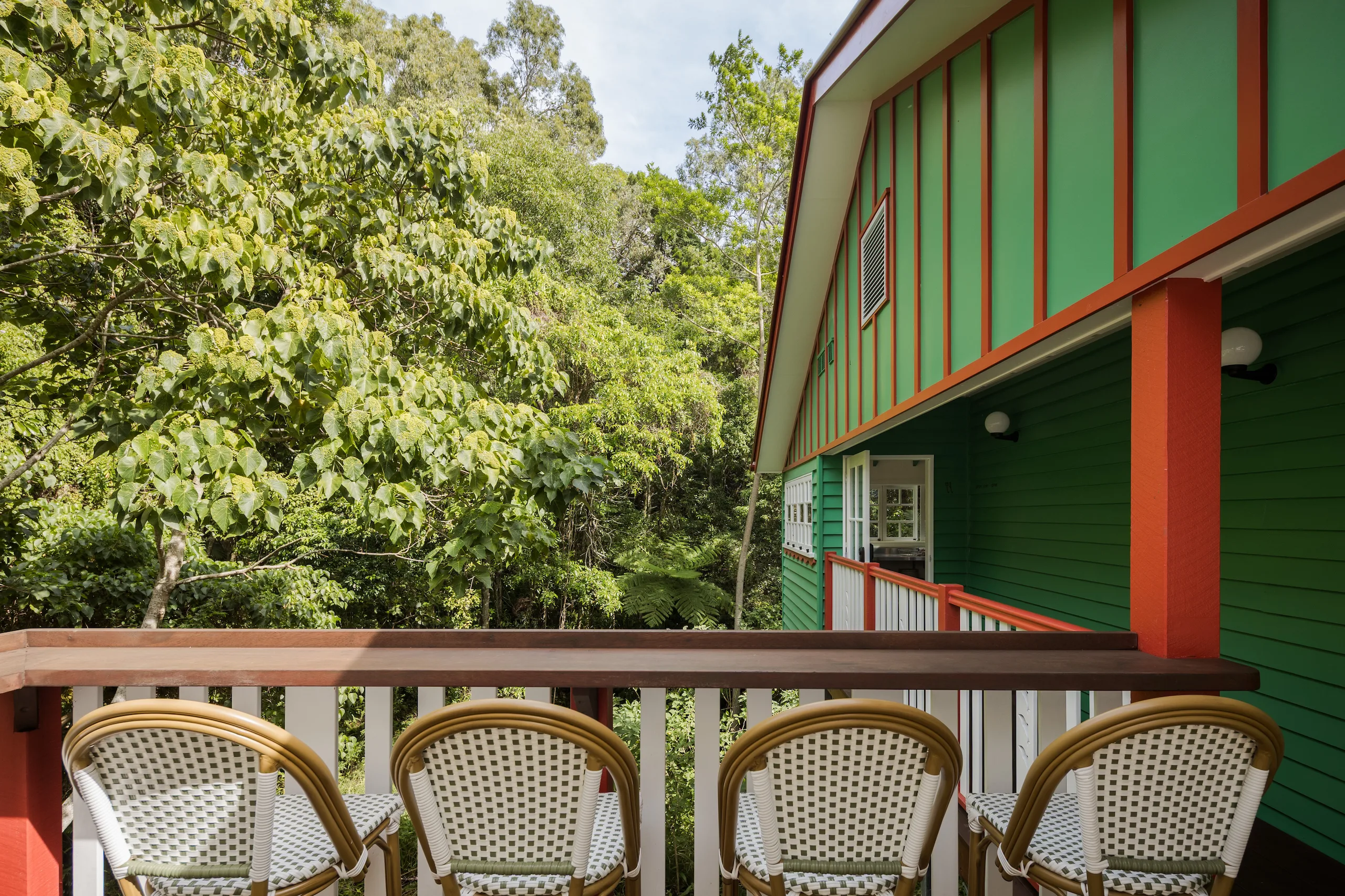 Green weatherboard balcony with rattan chairs overlooking dense rainforest canopy