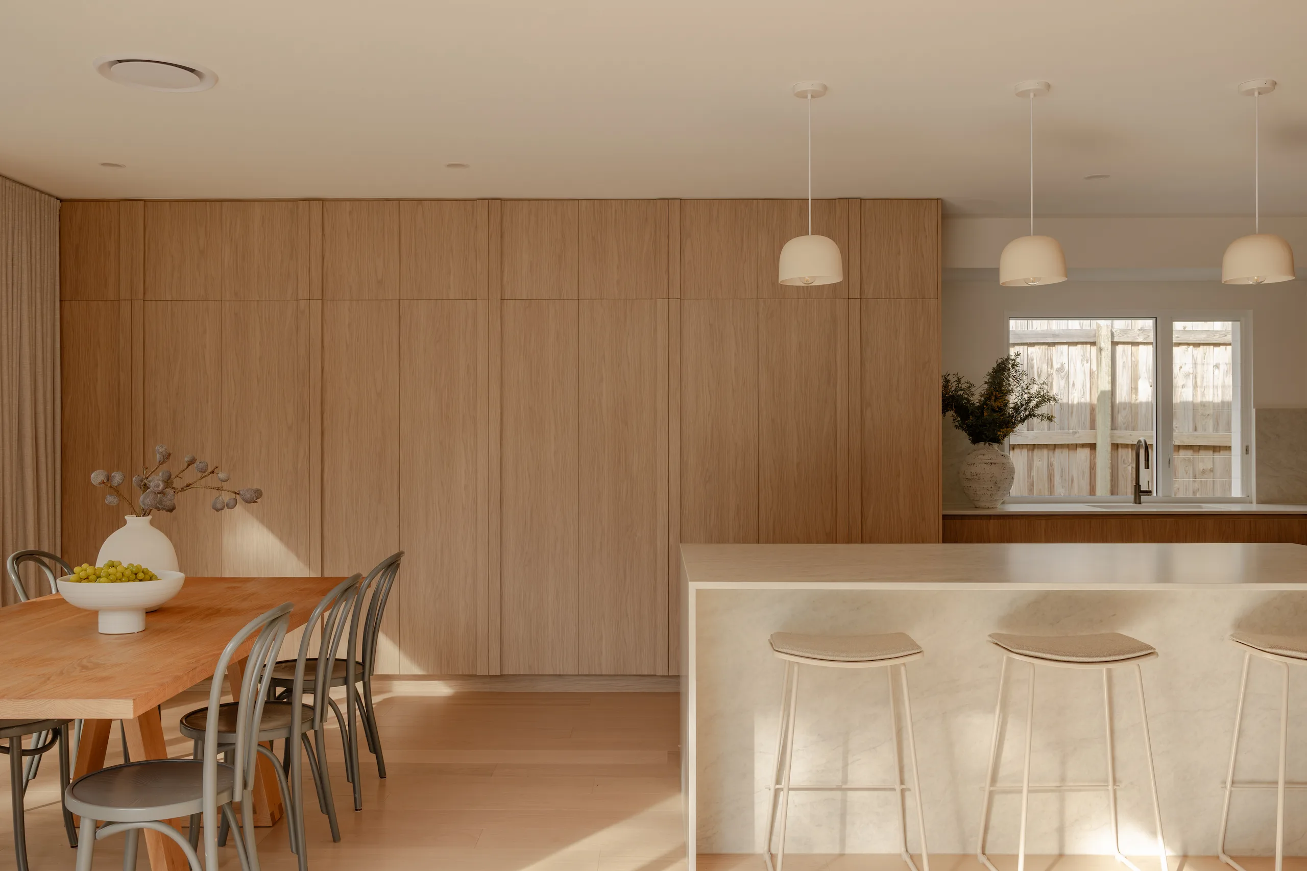 Open-plan kitchen and dining with timber panelling, pendant lights and stone island bench