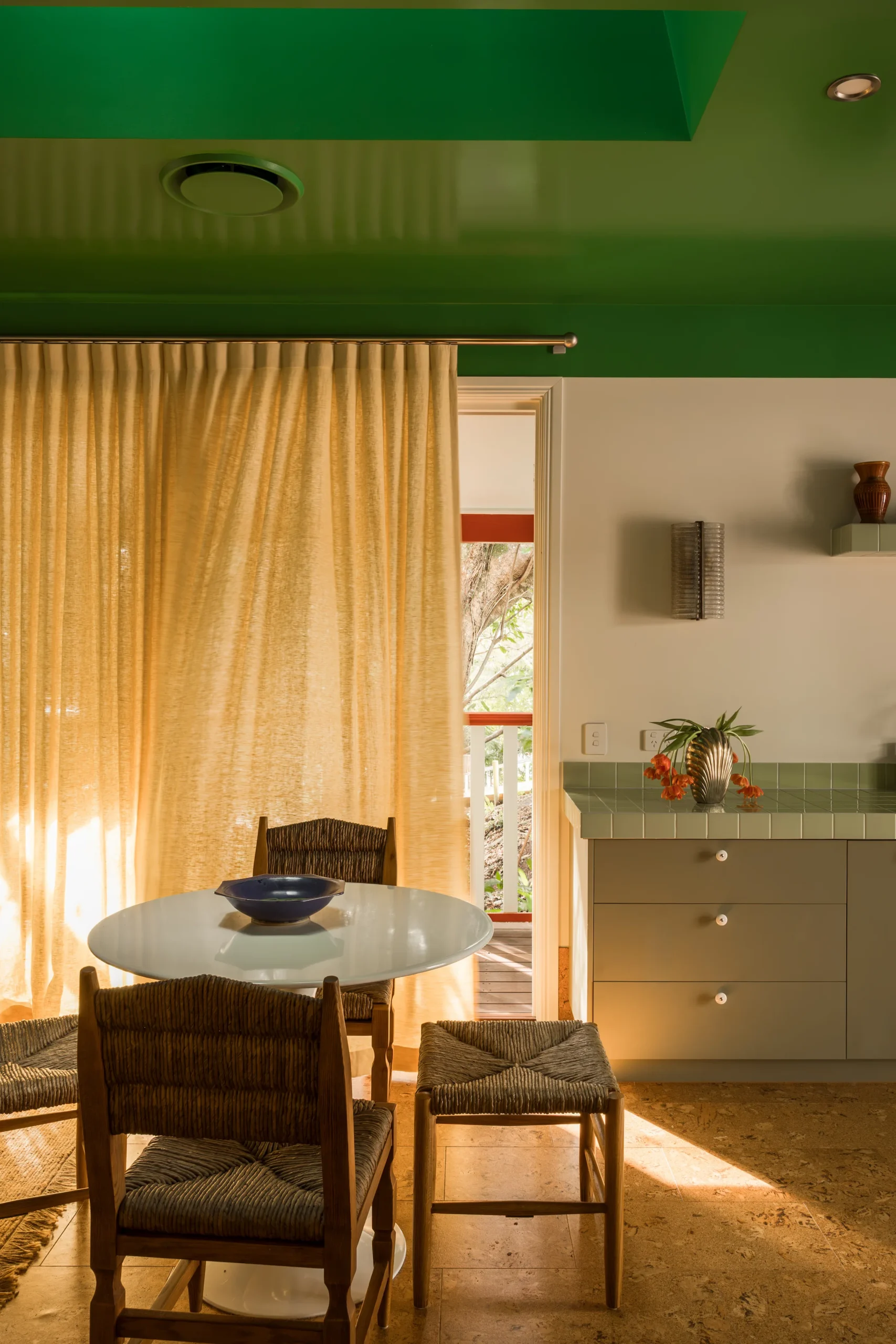Dining nook with mustard curtains, glass table and rattan chairs
