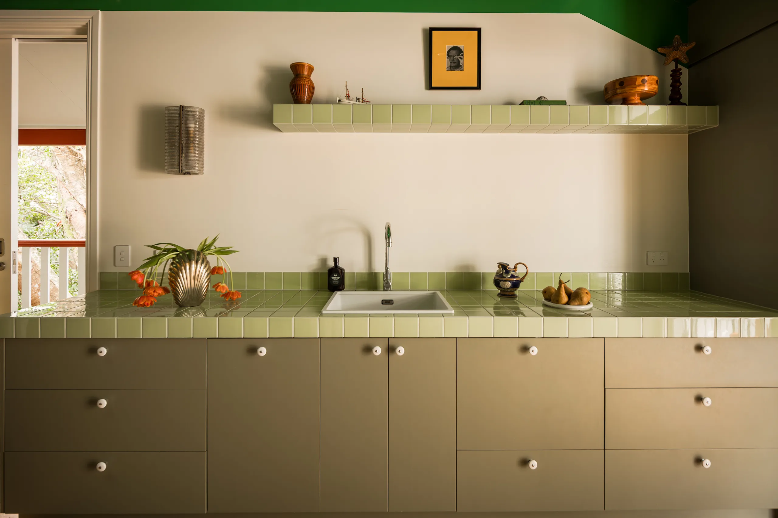 Green-tiled kitchenette splashback with sink, taps and decorative shelf