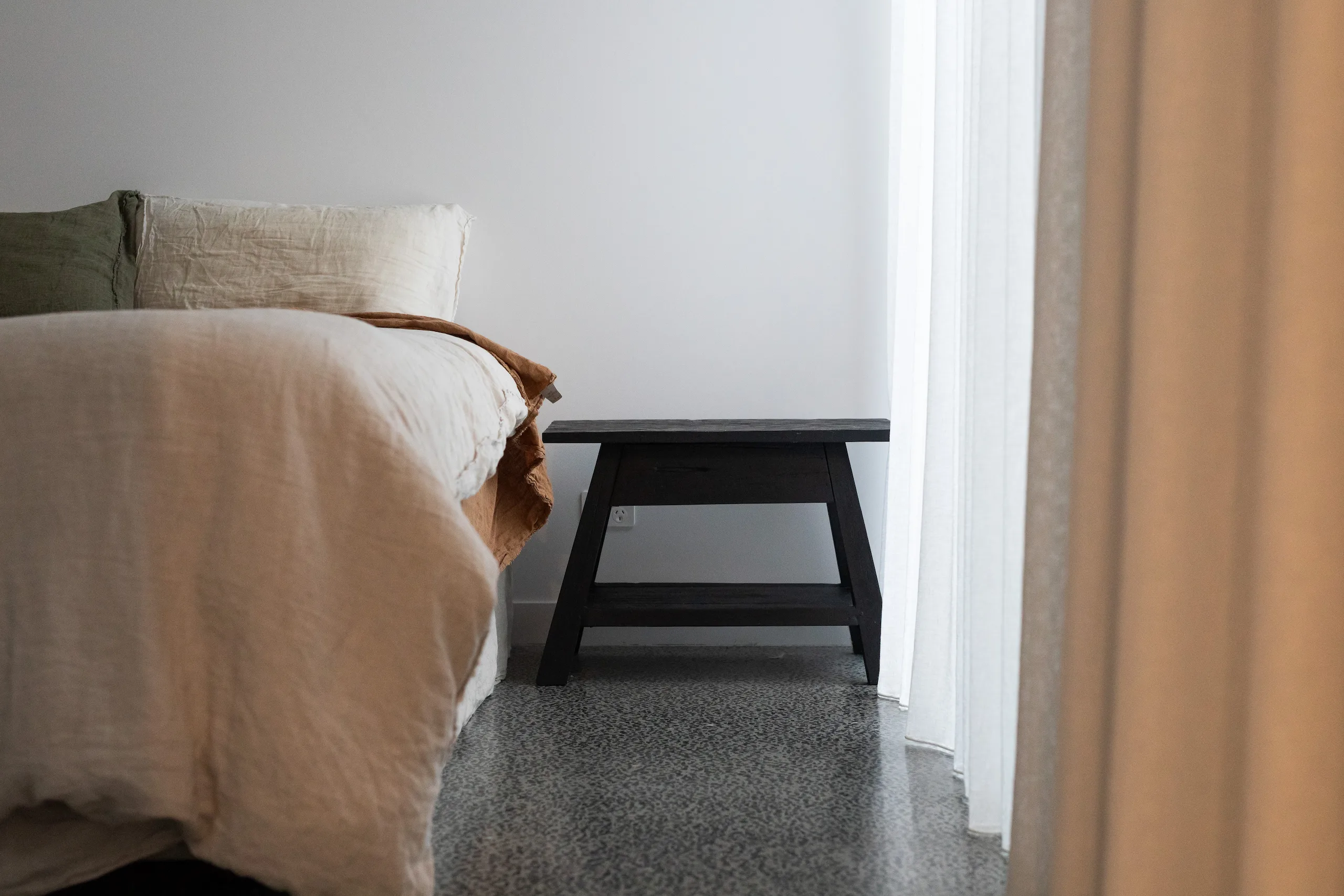 Bedside table on terrazzo floor beside linen-dressed bed