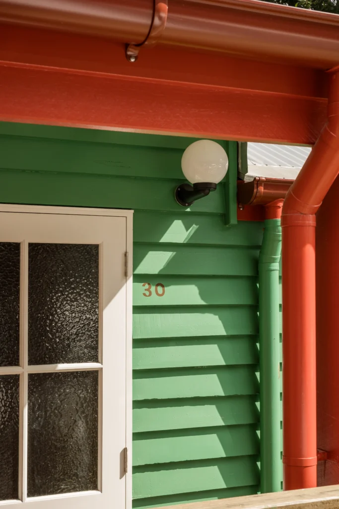 Green and red weatherboard exterior detail with house number and light fitting