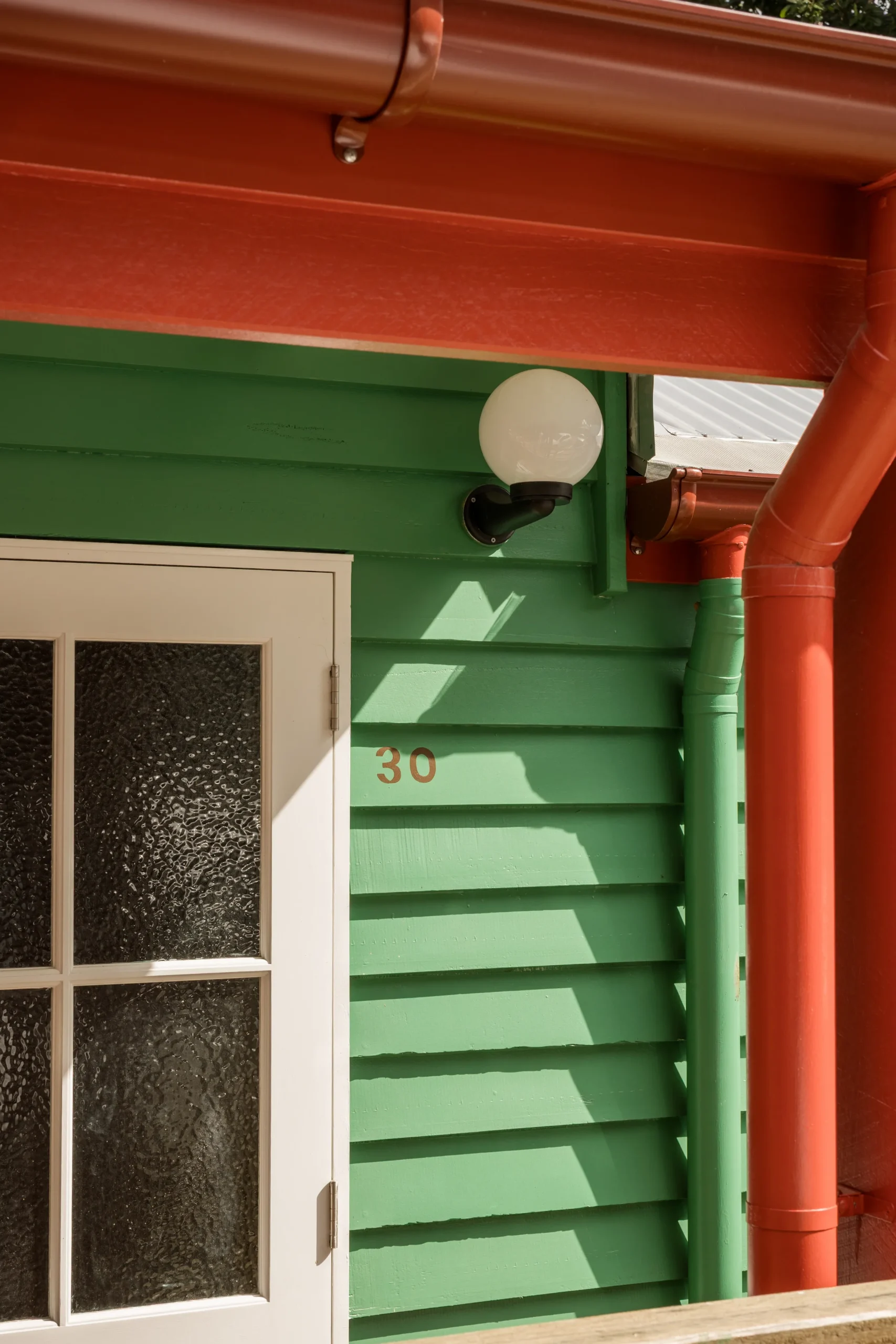 Green and red weatherboard exterior detail with house number and light fitting