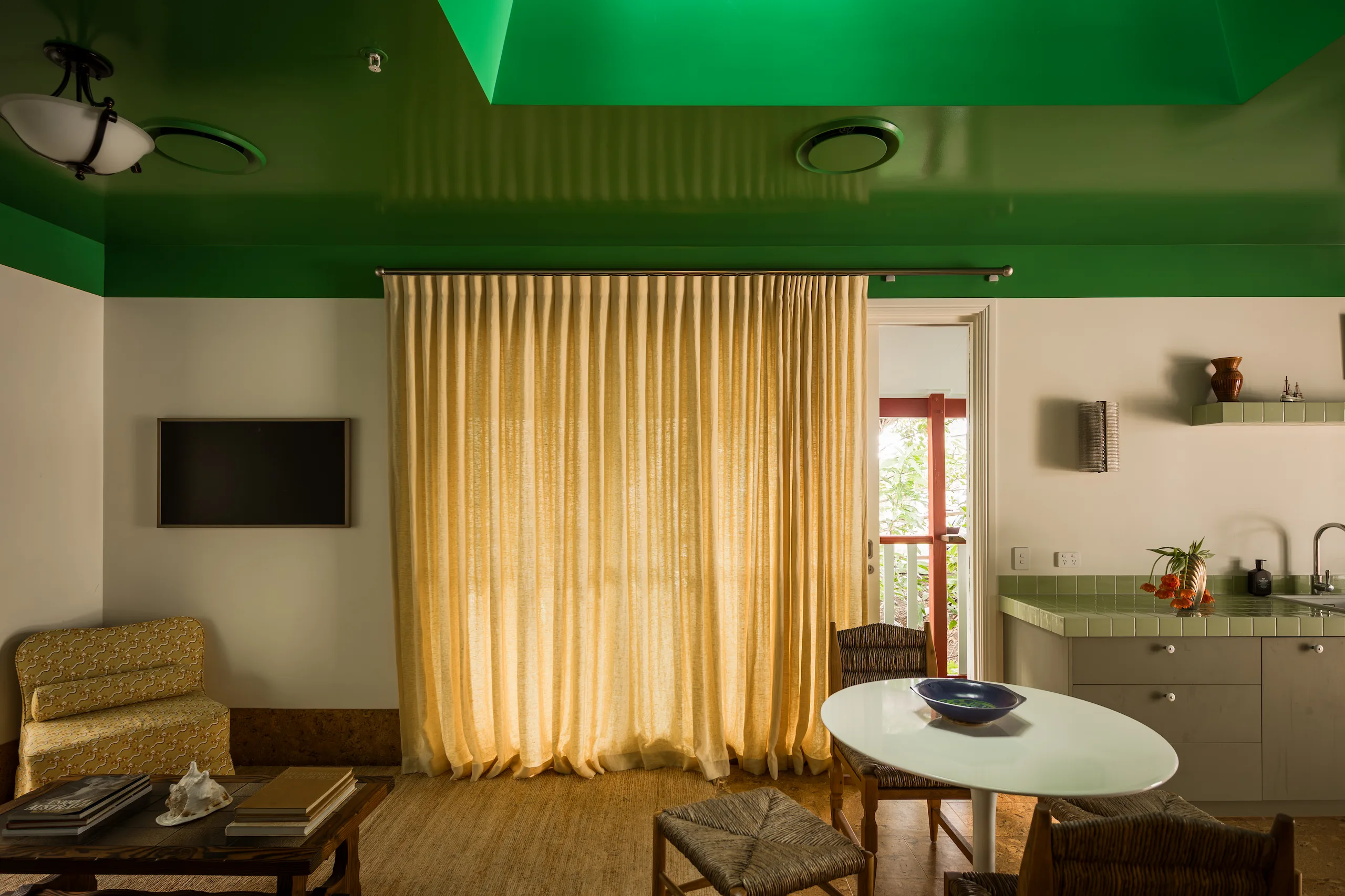 Green-ceilinged living room with mustard curtain and doorway to balcony