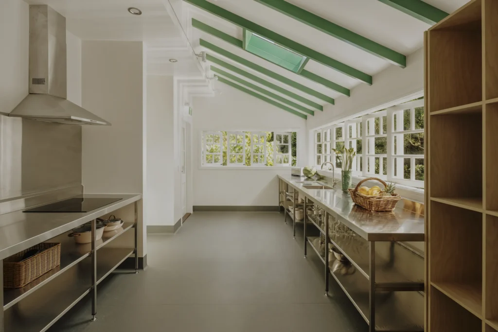 Green-beamed commercial kitchen with stainless benches and garden windows