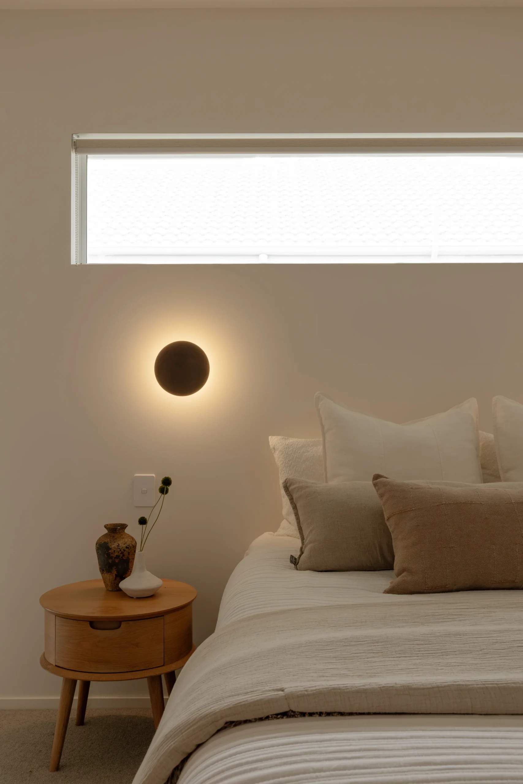 Bedroom wall sconce glowing beside a pillow-stacked bed